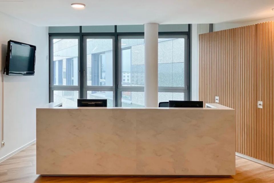 Moderner Empfangsbereich mit heller Theke, Holzlamellen und großen Fensterflächen